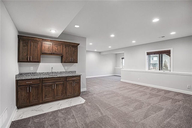 kitchen with light stone countertops, sink, light carpet, and dark brown cabinetry