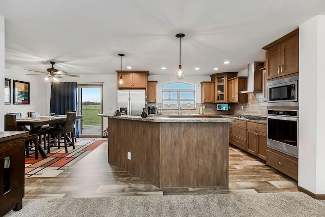 kitchen featuring appliances with stainless steel finishes, a center island, wall chimney exhaust hood, glass insert cabinets, and pendant lighting