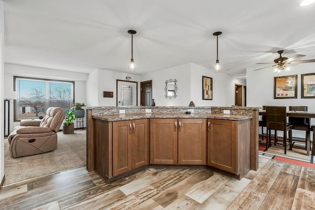 kitchen with light stone countertops, a kitchen island, pendant lighting, and brown cabinetry