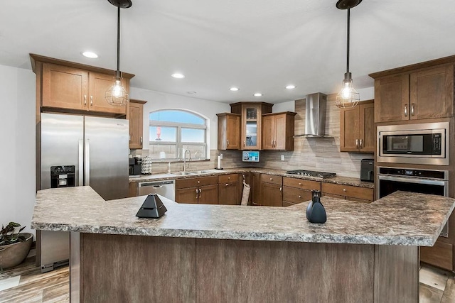 kitchen with brown cabinets, hanging light fixtures, appliances with stainless steel finishes, glass insert cabinets, and wall chimney range hood