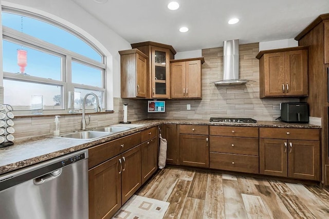 kitchen featuring a sink, appliances with stainless steel finishes, decorative backsplash, wall chimney exhaust hood, and glass insert cabinets