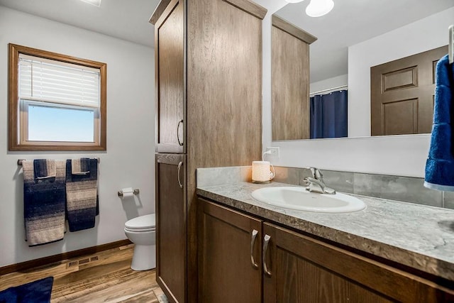 bathroom with visible vents, toilet, vanity, wood finished floors, and baseboards