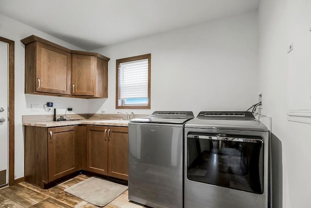 clothes washing area featuring light wood-style floors, a sink, cabinet space, and washer and dryer