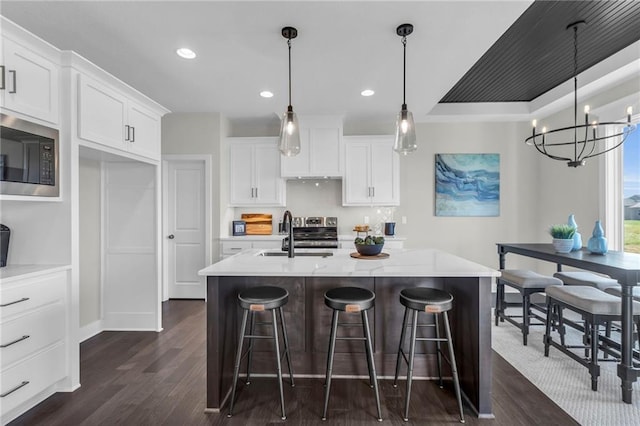 kitchen featuring built in microwave, an island with sink, sink, and white cabinets