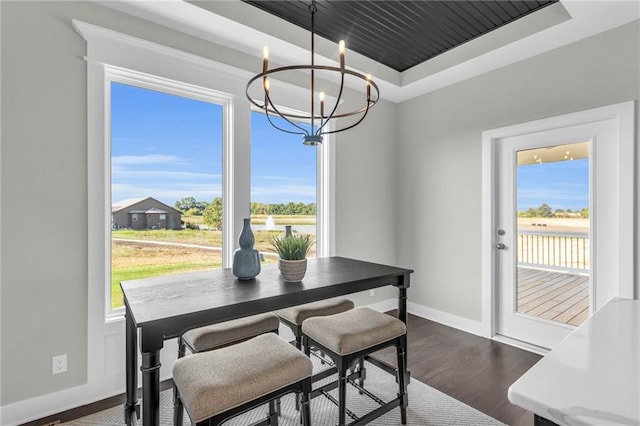 dining area featuring an inviting chandelier, a tray ceiling, and dark wood-type flooring