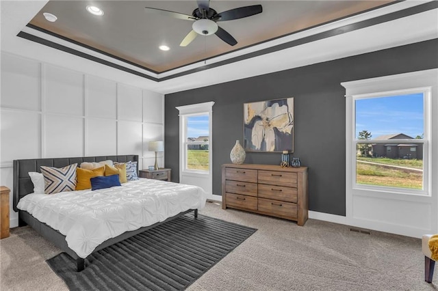 carpeted bedroom with ceiling fan and a tray ceiling