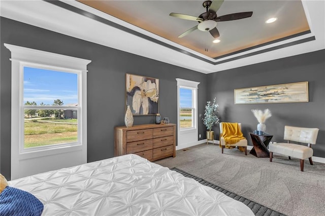 carpeted bedroom with ceiling fan, a raised ceiling, and multiple windows