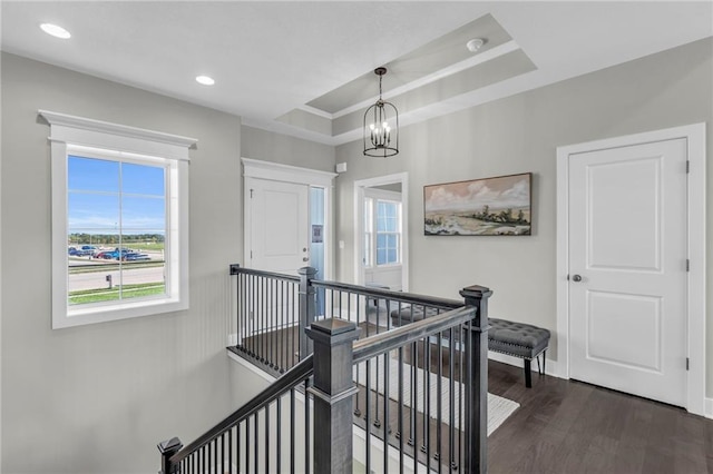 corridor featuring an inviting chandelier, a tray ceiling, and dark hardwood / wood-style floors