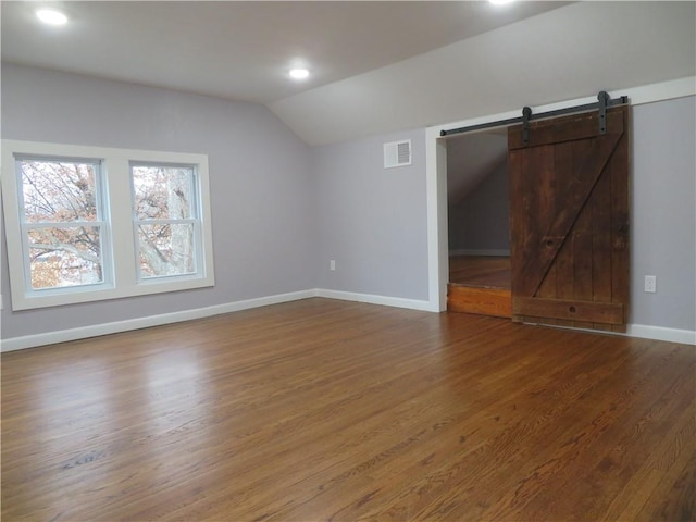 spare room with lofted ceiling, wood-type flooring, and a barn door