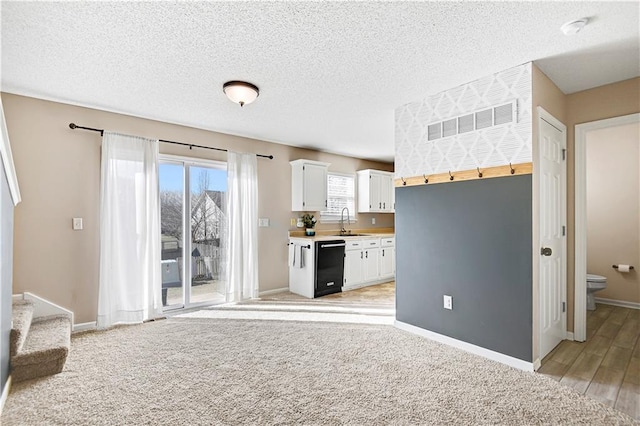 unfurnished living room featuring a textured ceiling, a sink, visible vents, baseboards, and stairs