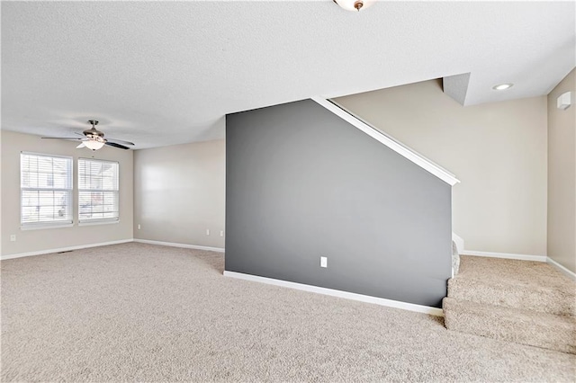 empty room with a textured ceiling, ceiling fan, carpet, and baseboards