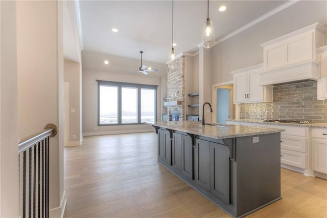 kitchen featuring hanging light fixtures, white cabinetry, a kitchen island with sink, and tasteful backsplash