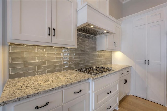 kitchen featuring premium range hood, white cabinetry, light stone counters, tasteful backsplash, and stainless steel gas stovetop