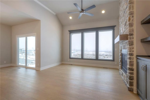 unfurnished living room featuring ceiling fan, a stone fireplace, vaulted ceiling, and light wood-type flooring