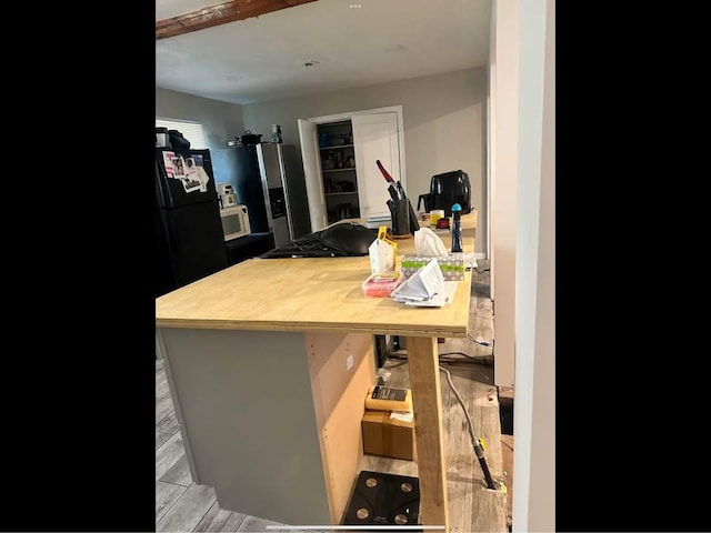 kitchen with white microwave, stainless steel refrigerator with ice dispenser, wood finished floors, and freestanding refrigerator