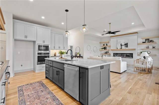 kitchen with decorative light fixtures, an island with sink, white cabinets, light stone counters, and stainless steel appliances