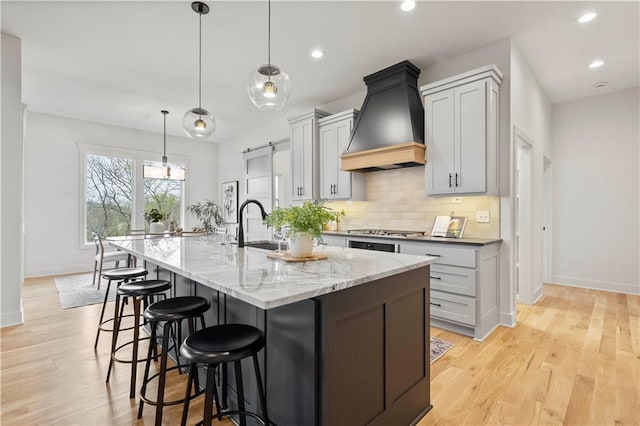 kitchen with a large island, gray cabinetry, light stone counters, decorative light fixtures, and custom exhaust hood