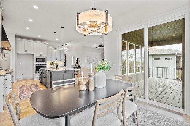 dining space featuring sink, ceiling fan with notable chandelier, and light hardwood / wood-style floors