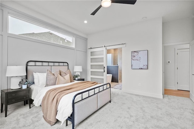 carpeted bedroom with a barn door, ceiling fan, and ensuite bathroom