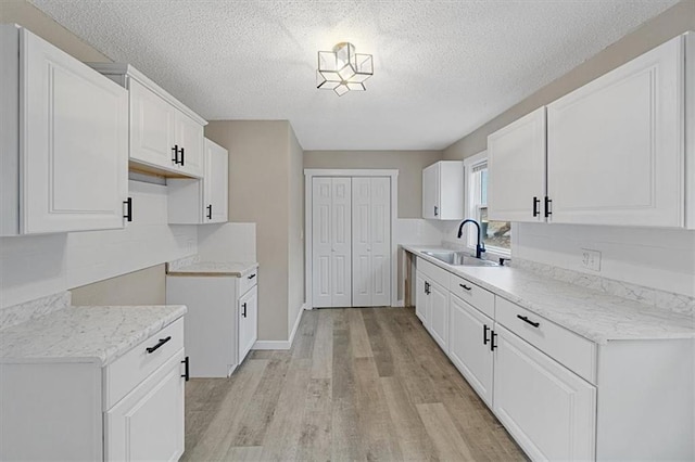 kitchen featuring light hardwood / wood-style floors, sink, a textured ceiling, and white cabinets