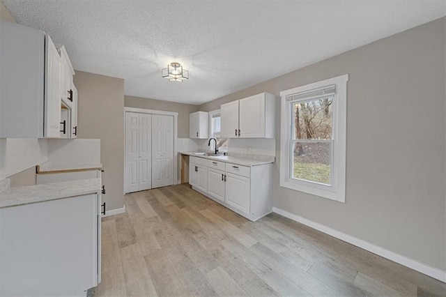 kitchen featuring sink, light wood-type flooring, a textured ceiling, and white cabinets