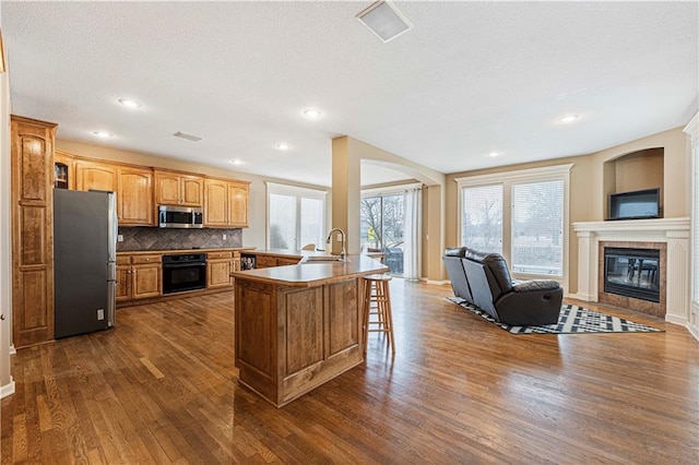 kitchen featuring a tile fireplace, stainless steel appliances, a sink, open floor plan, and a kitchen bar