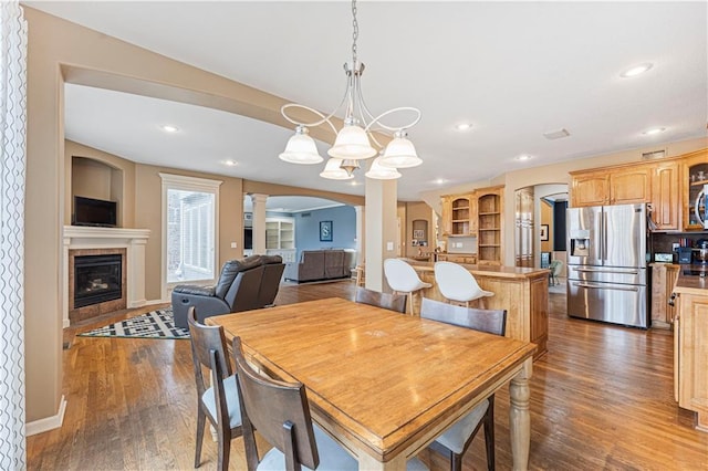 dining room featuring decorative columns, arched walkways, dark wood-type flooring, and a tile fireplace