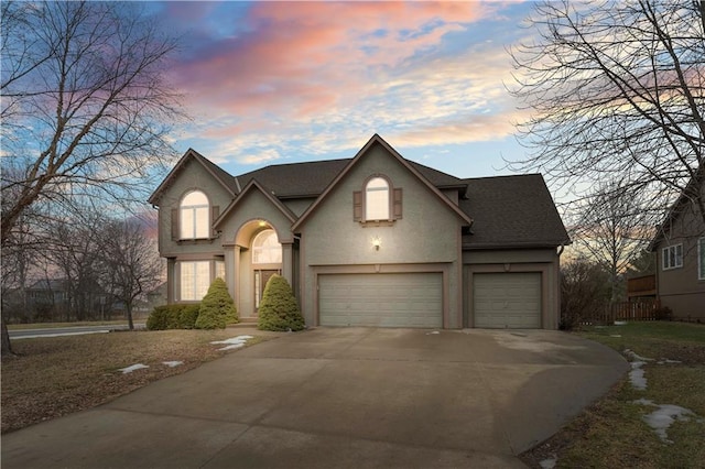 traditional-style house with stucco siding, an attached garage, concrete driveway, and roof with shingles