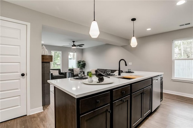 kitchen featuring pendant lighting, sink, dishwasher, dark brown cabinets, and a center island with sink