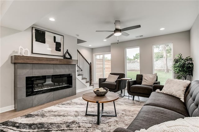 living room featuring ceiling fan, a tiled fireplace, and light hardwood / wood-style flooring