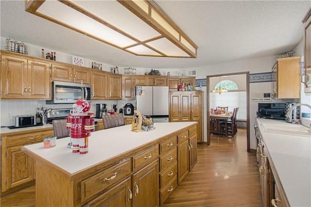 kitchen featuring sink, appliances with stainless steel finishes, a center island, light hardwood / wood-style floors, and a textured ceiling