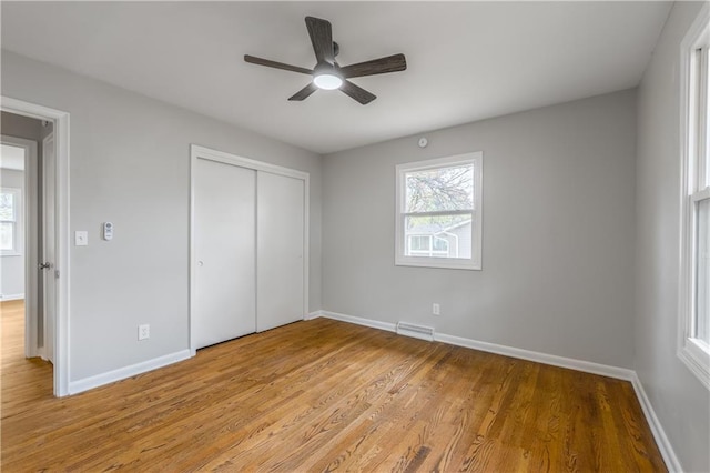 unfurnished bedroom featuring ceiling fan, a closet, multiple windows, and light wood-type flooring