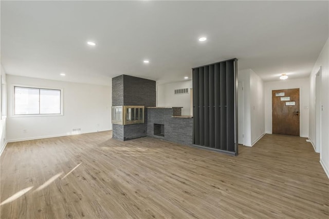 unfurnished living room featuring recessed lighting, a brick fireplace, baseboards, and wood finished floors