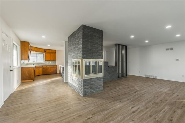 kitchen with light wood finished floors, light countertops, brown cabinetry, a brick fireplace, and open floor plan