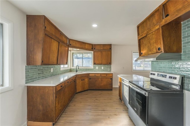 kitchen featuring under cabinet range hood, electric range, a sink, light countertops, and decorative backsplash