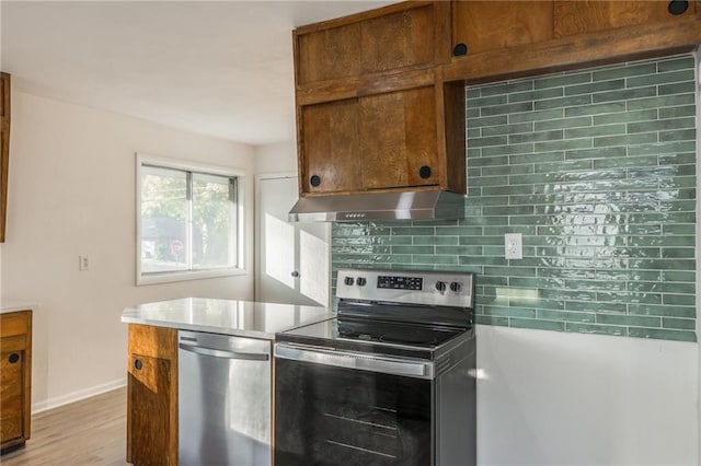 kitchen featuring stainless steel appliances, light countertops, backsplash, brown cabinetry, and under cabinet range hood