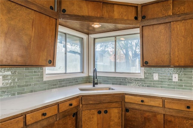 kitchen with light countertops, brown cabinetry, a sink, and decorative backsplash