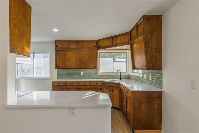 kitchen featuring a peninsula, brown cabinetry, light countertops, and a sink