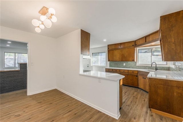 kitchen with a peninsula, light countertops, light wood-type flooring, backsplash, and brown cabinets