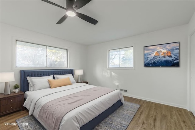 bedroom featuring a ceiling fan, visible vents, baseboards, and wood finished floors