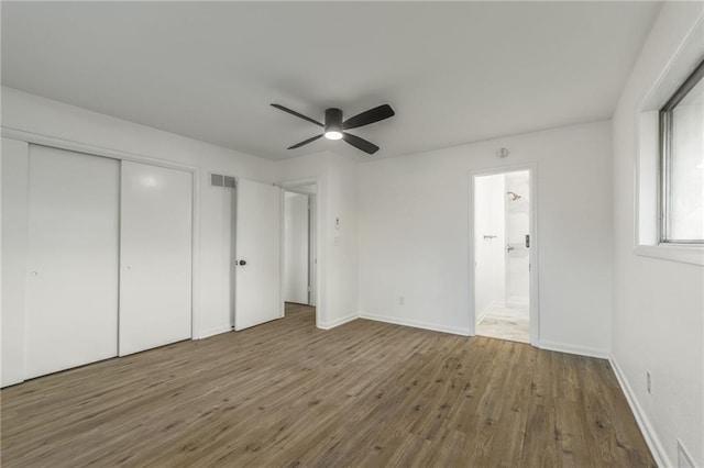 unfurnished bedroom with a closet, wood finished floors, visible vents, and baseboards