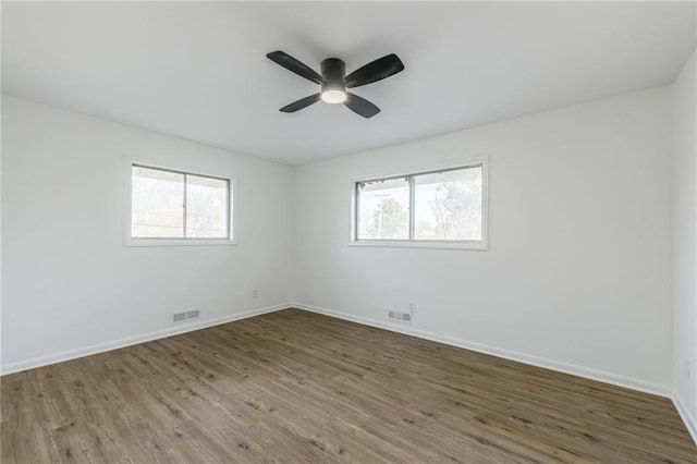 empty room with a ceiling fan, visible vents, baseboards, and wood finished floors