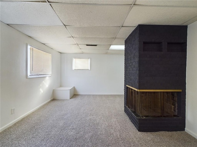 basement featuring a fireplace, baseboards, a drop ceiling, and carpet flooring