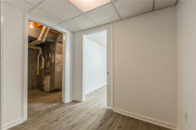 interior space with heating unit, a paneled ceiling, baseboards, and wood finished floors