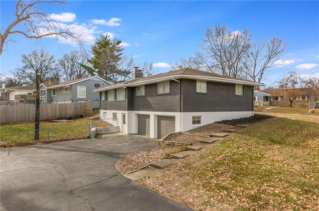 view of side of property with driveway, a chimney, an attached garage, fence, and brick siding