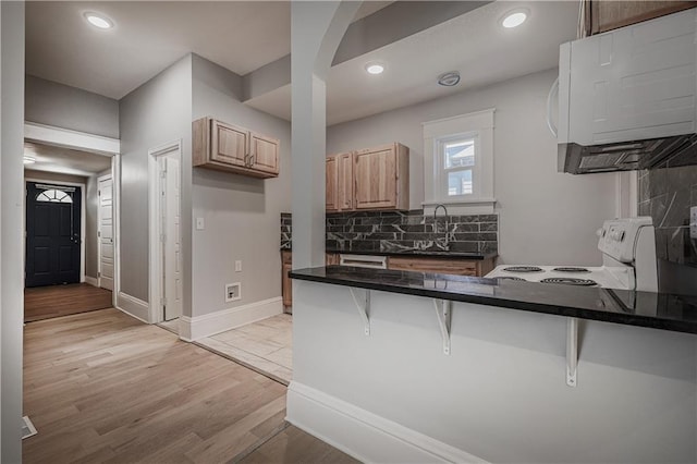 kitchen with backsplash, a kitchen bar, electric range, light hardwood / wood-style floors, and kitchen peninsula