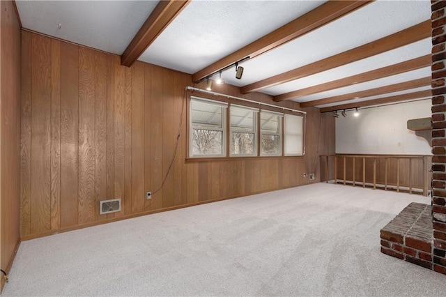 unfurnished living room with beamed ceiling, rail lighting, carpet floors, and wood walls