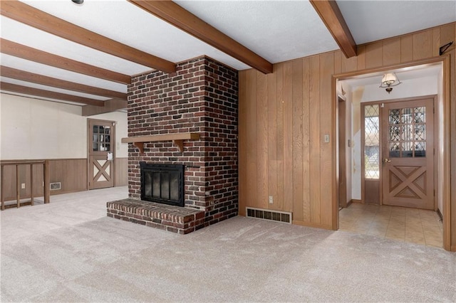 unfurnished living room featuring beamed ceiling, carpet flooring, a fireplace, and wood walls