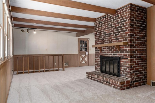 unfurnished living room featuring light carpet, a brick fireplace, beam ceiling, and wood walls