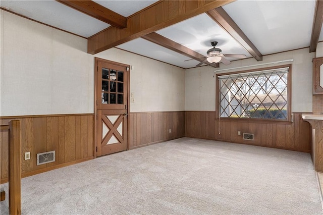 spare room with ceiling fan, wooden walls, light carpet, and beam ceiling